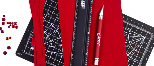 a craft knife, ruler, and red construction paper on a cutting mat