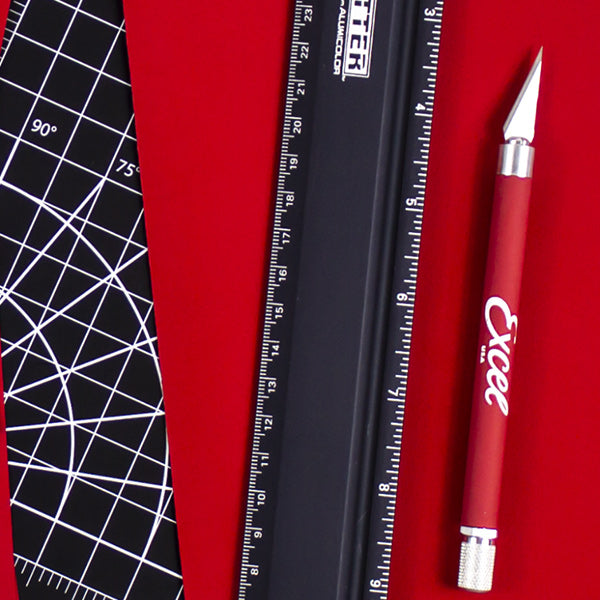 a craft knife, ruler, and red construction paper on a cutting mat