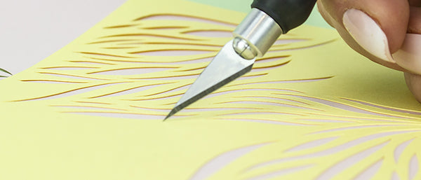 a person using a hobby knife to cut designs in paper
