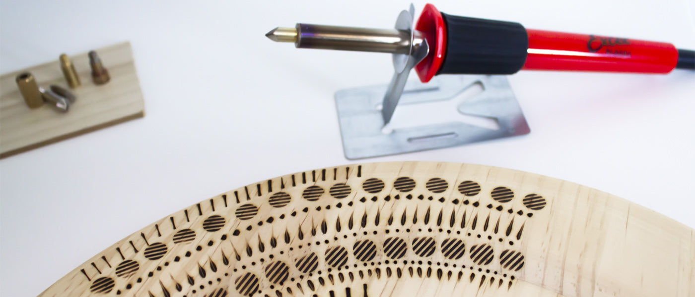 a pyrography pen next to a piece of wood with burned in designs