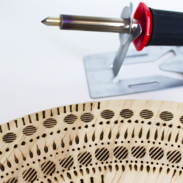 a pyrography pen next to a piece of wood with burned in designs